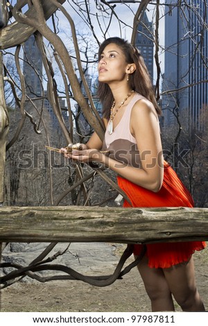 A pretty woman is holding an egg nest and hopefully looking up. The background is small woods, vine tree and high building skyline/Looking for Home