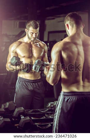 Young adult man doing bicep curls in modern gym.