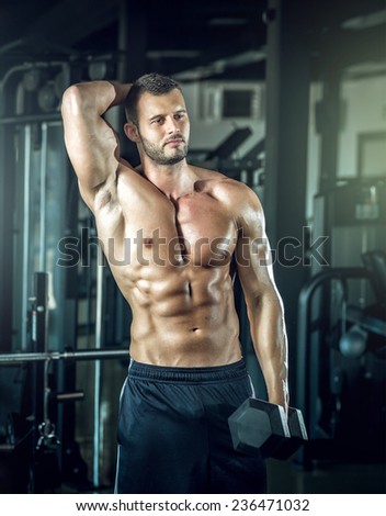 Young adult man doing bicep curls in modern gym.