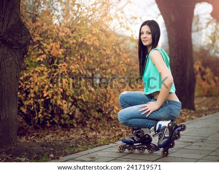 Young adult girl kneeling on roller skates in park during autumn season.