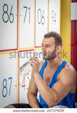Young adult tired man drinking water in locker room of gym.