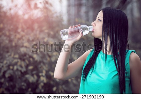 Young adult girl drinking water from bottle in park.