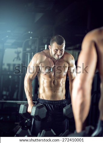 Young adult man doing bicep curls and posing in gym
