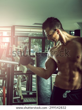 Young adult teenage man doing dumbbell biceps curls in gym