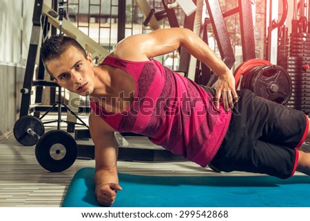 Young teenage guy doing side plank exercise in gym.