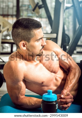 Man posing on gym floor with protein shake mix.