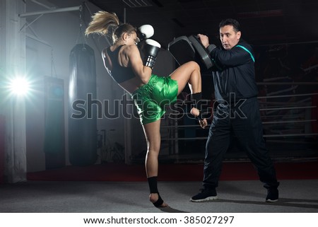 Girl doing knee kick exercise during kickboxing training with personal trainer