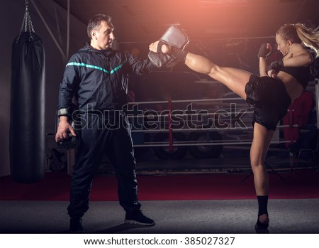 Young adult sexy woman doing back leg high kick during kickboxing exercise with trainer