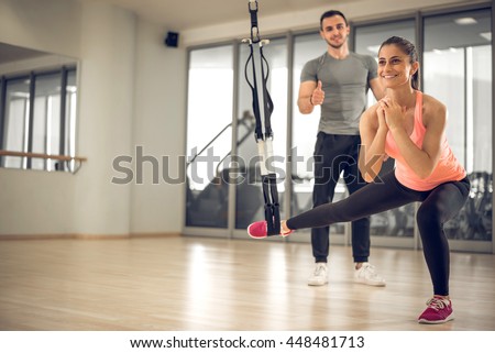 Young adult girl doing suspension rope exercise together with her personal private coach.