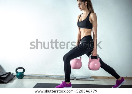 Attractive fit female doing lunge fitness exercise with pink rose kettlebell weight.