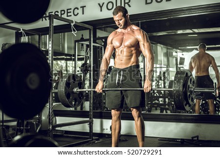 Attractive tall muscular bodybuilder doing heavy deadlifts in moder fitness center. Toned image.