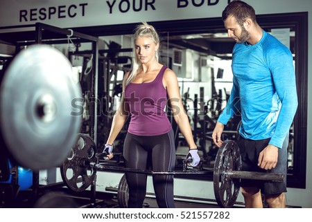 Attractive blonde woman doing trap bar deadlift exercise with help of her personal trainer. Toned image.