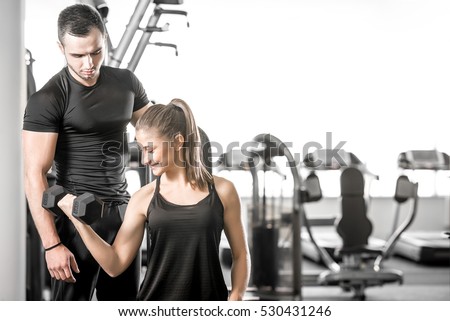 Young adult woman working out in gym, doing bicep curls with help of her personal trainer.