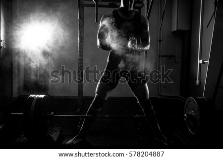 Young adult fit athlete preparing to do sumo deadlift exercise using powder for better hand grip.