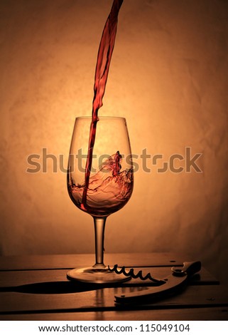 Red wine splashing into small glass . Wine composition with warm back light.