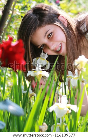 Pretty girl smiles with braces through de-focused flowers. Natural light portrait