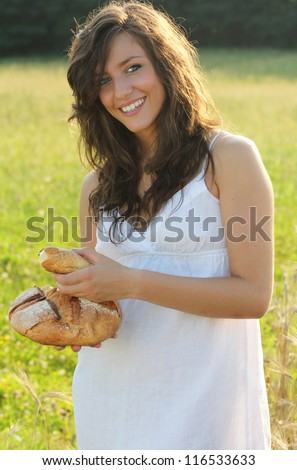 Happy and smiling girl with white country dress and beautiful piece of bread in hands.
