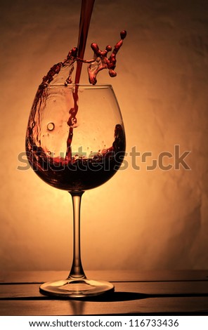 Red wine splashing into large and elegant  wineglass . Composition with warm back light.