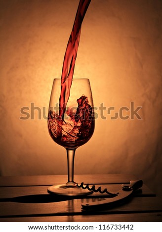 Red wine splashing into small wineglass .  Composition with warm back light