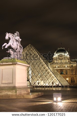 PARIS - OCTOBER 11: Louis XIV statue and lighted glass pyramid of Louvre museum on October 11, 2012 in Paris, France .Louis XIV is also known  as Louis the Great or the Sun King