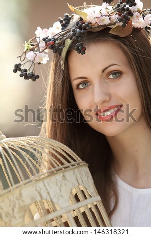 Beautiful spring nymph portrait with vintage bird cage. Model wearing a flowers crown
