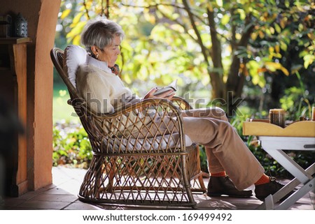 Senior lady reading a book outdoor , comfortably seated in the garden . Relax concept