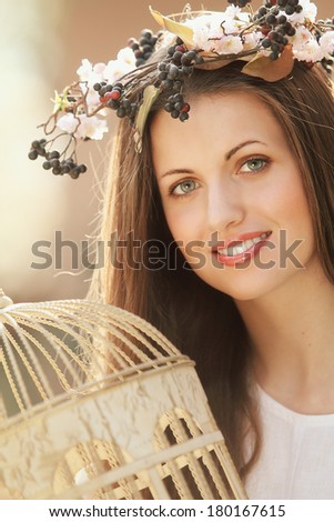 Beautiful spring nymph portrait with vintage bird cage. Model wearing a flowers crown