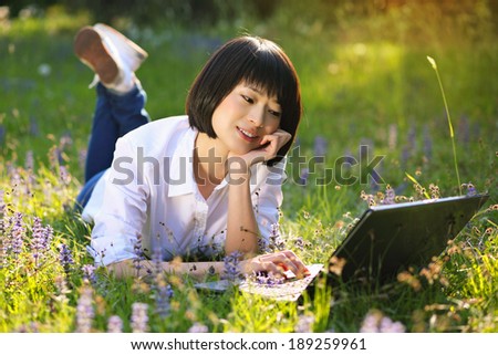 Attractive chinese girl using laptop among flowers . Outdoor work and study
