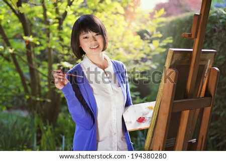 Smiling girl painting a canvas outdoor in the garden . Creativity and relax