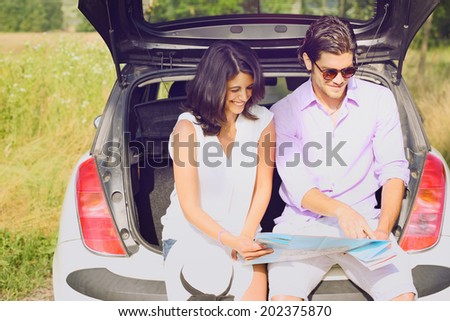 Smiling tourists with a road map  in the car boot . Holiday and journey
