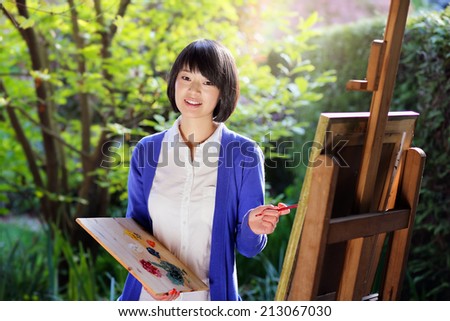 Happy young woman painting a canvas in the garden . Creativity and relax