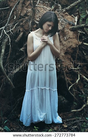 Beautiful woman with eyes closed praying among dead trees . Dark fantasy