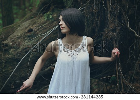Young woman among tree roots . Dark portrait in the forest