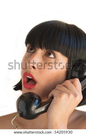 A young woman holds the telephone surprised at what she\'s listening from the other side, on white background