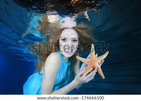 Beautiful woman smiling underwater in the pool with sea star