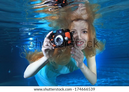 Woman smiling underwater in the pool with photo camera