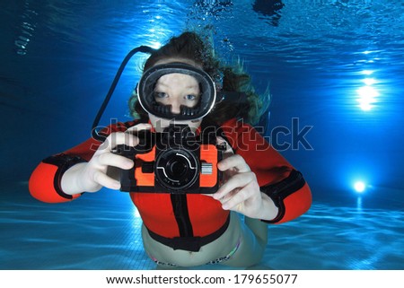 Scuba woman with camera and red neoprene suit underwater in the pool