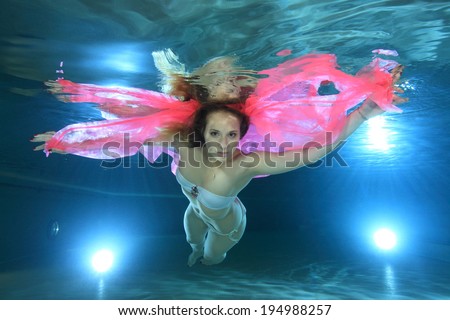 Young woman underwater in the pool floating with pink foulard