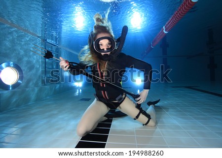 Scuba woman with black neoprene dress and spear gun diving underwater