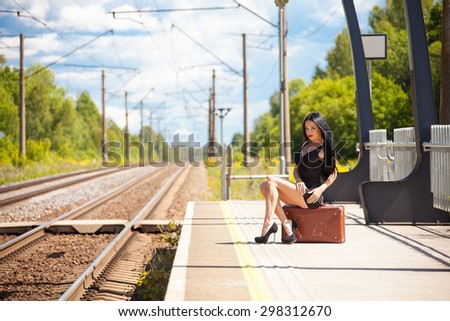 Beautiful young woman with luggage is waiting for a train on the train station