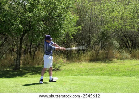 Golfer in striped shirt hitting the ball from the tee box. Golf club and arms of the golfer are in motion.
