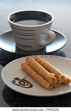 A white cup of coffee on black saucer. Next to it are baked swirls filled with cream and decorated with chocolate sauce. Shallow Depth of Field.
