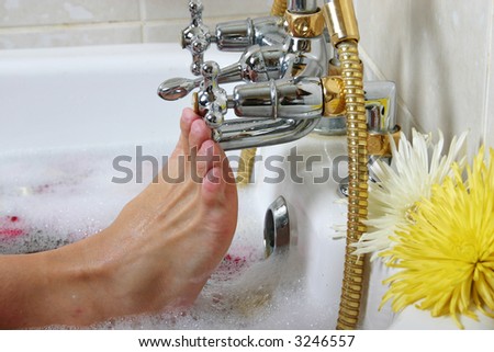 Foot of Caucasian woman touching the tap in the bath full of bubbles