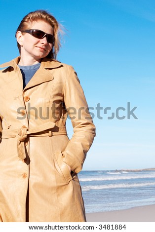 Blonde woman in a leather coat and sunglasses smiling. Blue sky in the background.