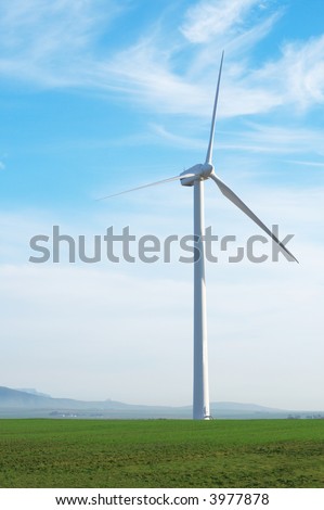 Wind powered electricity generator standing against the blue sky in a green field on the wind farm