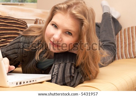 Blonde woman in casual clothes lying on the couch and working on her laptop
