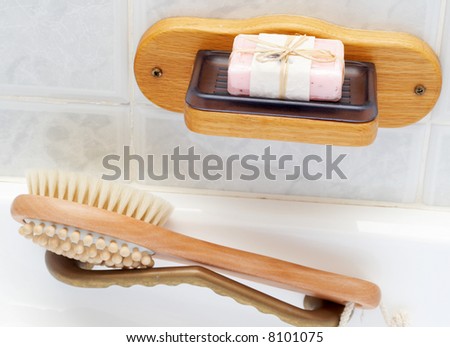 Relaxing spa scene with exfoliating brush massager and pink handmade soap in plastic soap dish