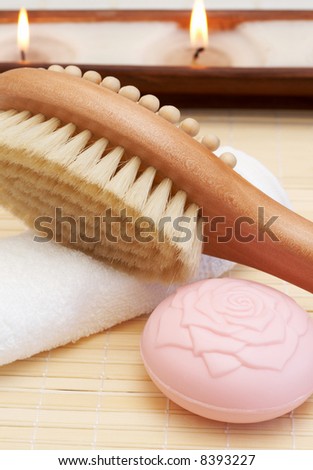 Relaxing spa scene with body brush massager, soap, white towel and candles in the background