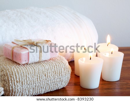Relaxing spa scene with white fluffy towel, body sponge and handmade soap with candles in the background