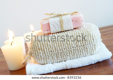 Relaxing spa scene with exfoliating body sponge, handmade soap, white face cloth and candles in the background